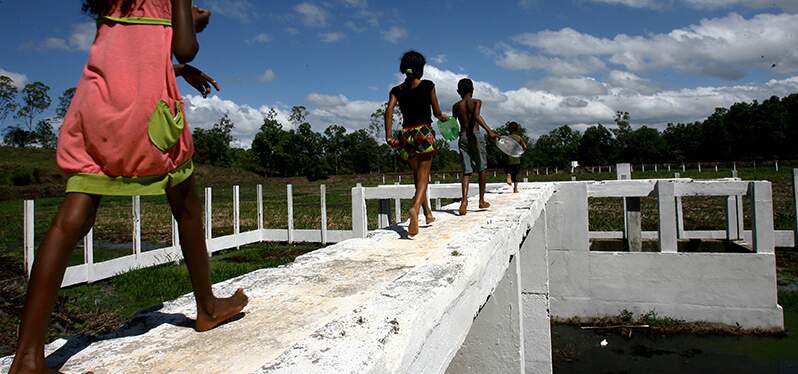 Crianças atravessam uma viga de concreto, com uma paisagem verdejante ao fundo