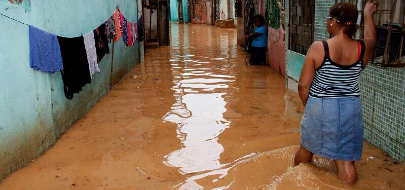 Uma mulher aparece atravessando uma rua inundada por água suja