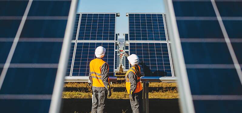 Duas pessoas aparecem trabalhando numa obra de painéis solares