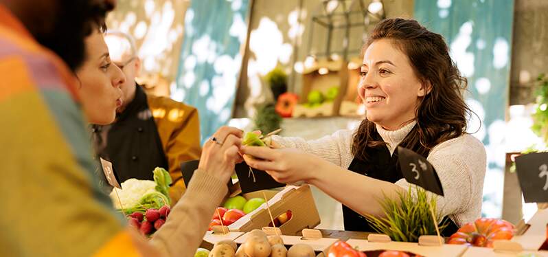 Mulher oferecendo um alimento aos clientes em uma espécie de feira